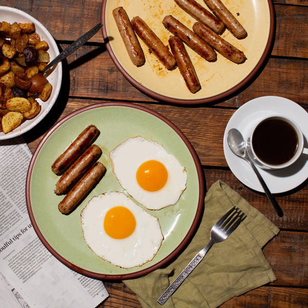 Breakfast Sausage in a plate with egg. A cup of Coffee, extra plate of sausages and Potato skillet on the side.