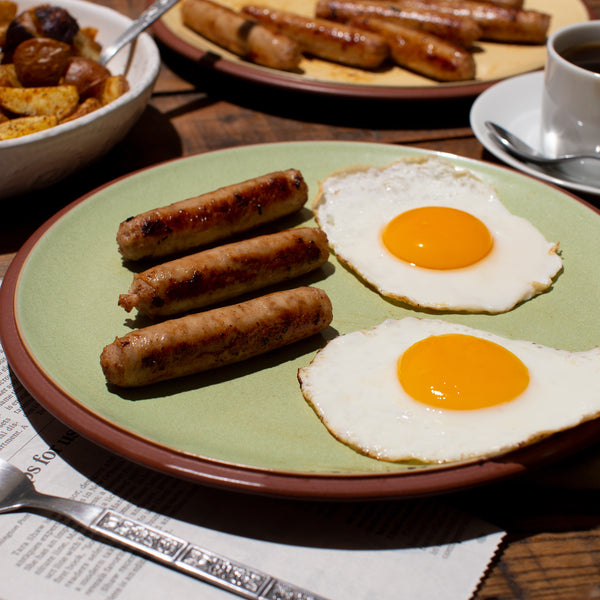 Breakfast Sausage in a plate with egg. A cup of Coffee, extra plate of sausages and Potato skillet on the side.